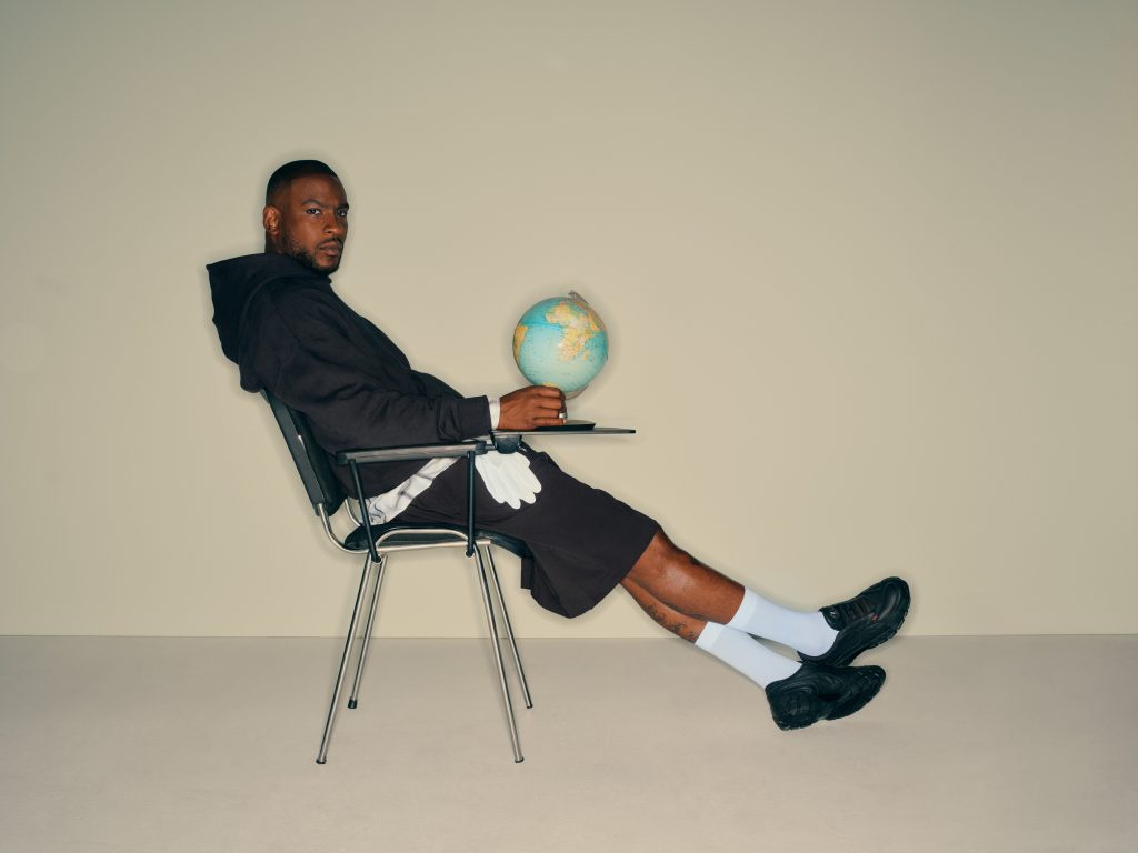 Skepta holding globe, sat on chair