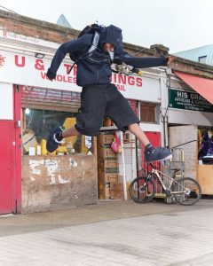 A man suspended in mid air, wearing a futuristic black outfit designed by Yaku in collaboration with Nike Re-Create