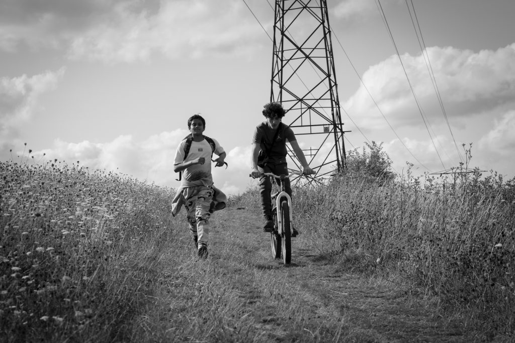 Photograph of two 12 year old boys in the countryside in the summer holidays. One is riding a bicycle and the other is running beside him. Screen grab from movie Ish, released in cinemas in July 2026.