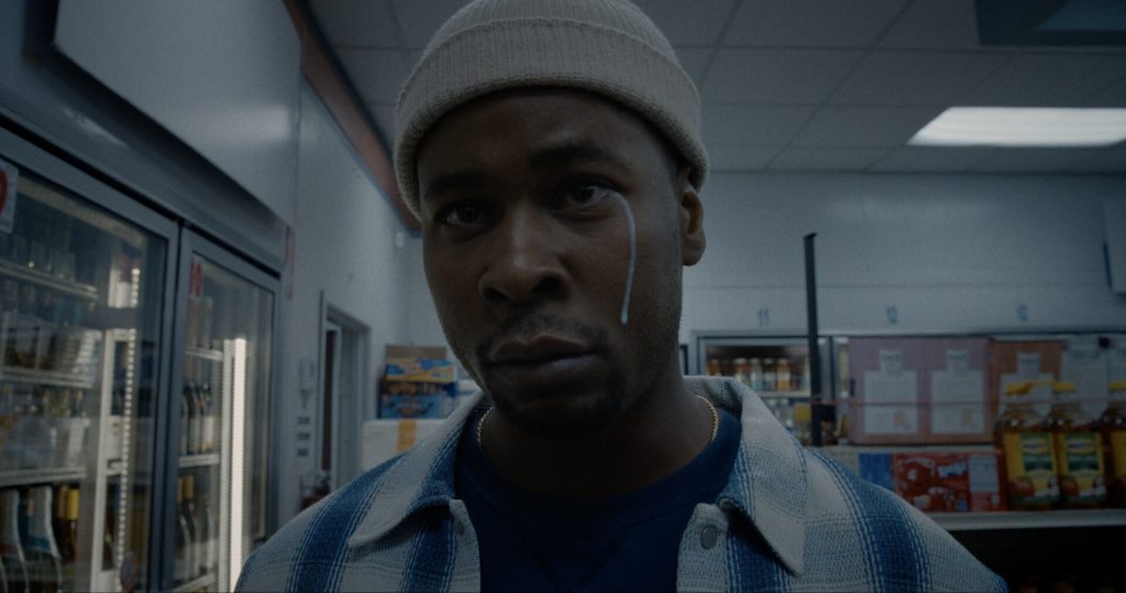 A photograph of a black man wearing a hoodie, with a tear made from milk