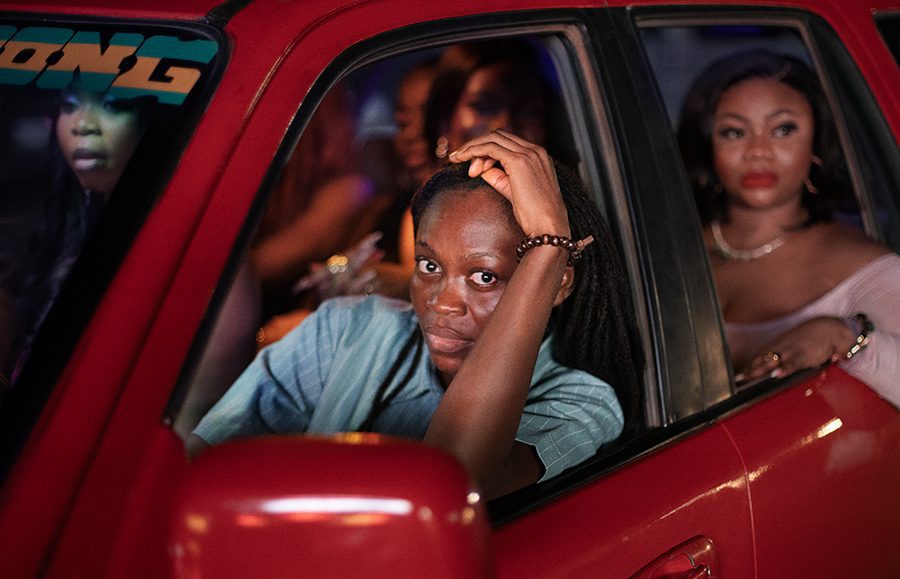 Photograph of a female taxi driver in a red car, with passengers.
